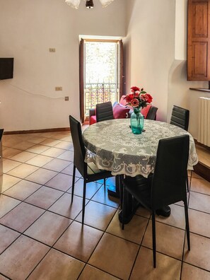 A dining area with a round table, chairs, a vase with flowers, and a view through a door to an outdoor balcony.