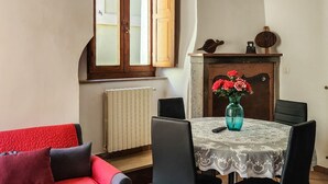 A dining area with a table set for four, a red sofa, and a fireplace with a vase of flowers.