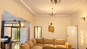 A living room with a sectional sofa, a dining table, a chandelier, and a view through a glass door.