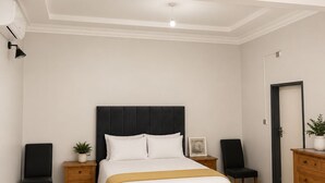 A bedroom with a bed, bedside tables, a dresser, a door, and a ceiling light.