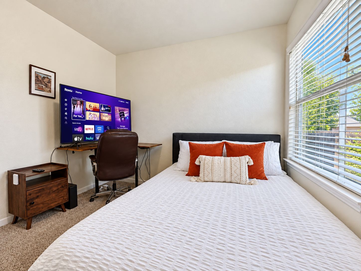 Ein Schlafzimmer mit einem Bett, einem Schreibtisch mit Computer und einem Fenster mit Jalousien.