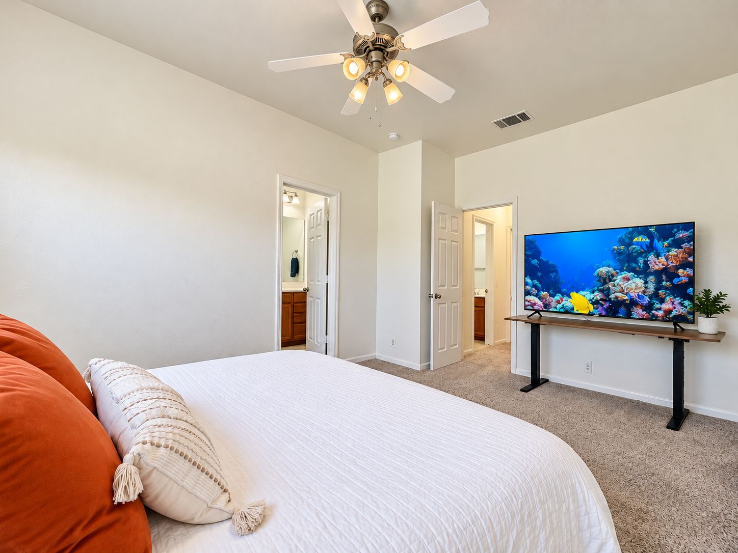 A bedroom with a bed, a ceiling fan, a television, and an open door leading to a bathroom.