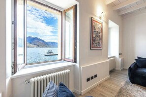 Ein Zimmer mit großem Fenster und Seeblick, einer Heizung, einer schwarzen Couch und einem gerahmten Bild an der Wand.