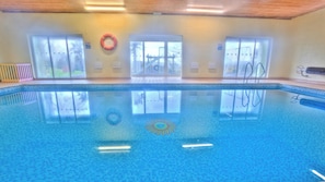 An indoor swimming pool with clear glass walls, a lifebuoy, and a view of a bridge outside.