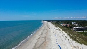 Ein Strand mit weitem Sandstreifen, einigen Gebäuden und einem klaren, blauen Himmel.