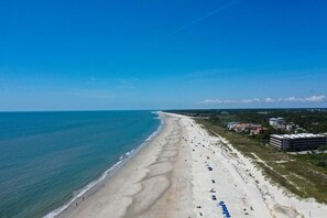 A beach with a long stretch of sand, a few buildings, and a clear blue sky. - Updated Luxury 3 BR Oceanfront Sea Cloisters New Kitchen & Baths Bike Rentals (Hilton Head Island)