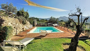 Una piscina con lettini, una zona barbecue e vista sulle montagne.