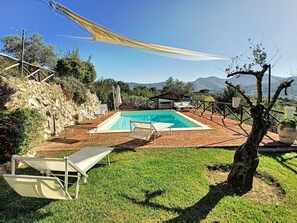 Una piscina con sillas de descanso, zona de barbacoa y vistas a montañas.