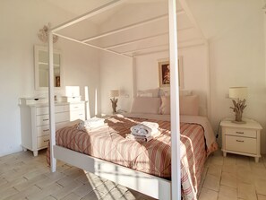 Una cama con dosel, un edredón a rayas, una mesita de noche con lámpara, un aparador y un espejo.
