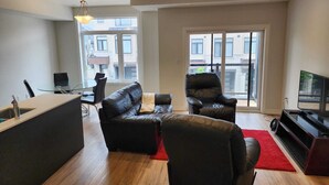 Ein modernes Wohnzimmer mit einer Couch, einem Sessel, einem Fernseher und einem Glastisch.