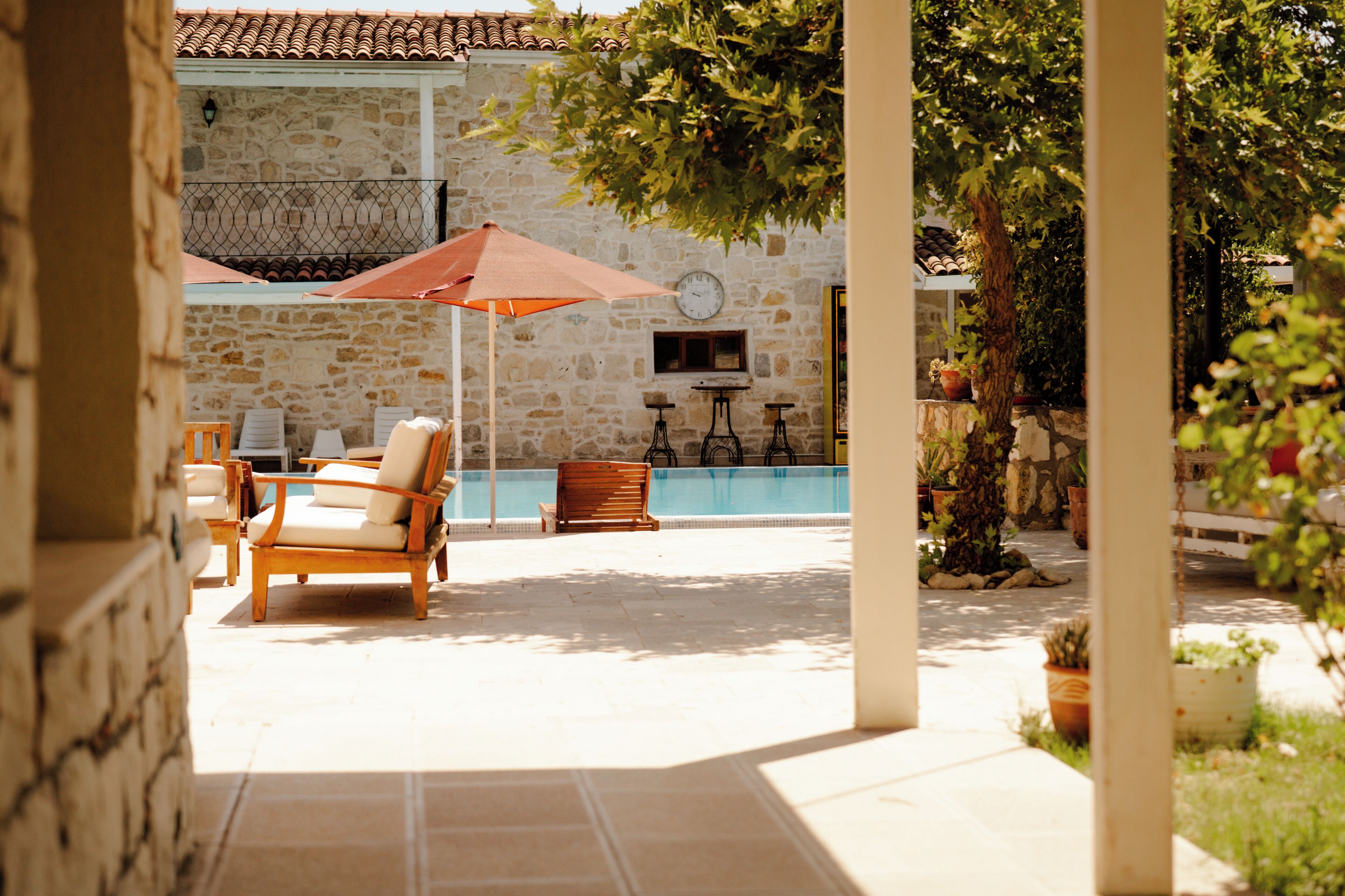 Zona de piscina con sillones reclinables, una mesa y una sombrilla grande.