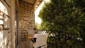 Balcón con muro de piedra, una mesa y sillas, con vistas a un jardín de follaje denso.