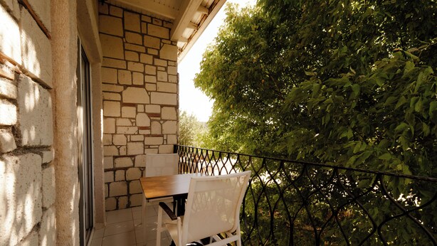 Balcón con muro de piedra, una mesa y sillas, con vistas a un jardín de follaje denso.