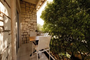 Balcón con muro de piedra, una mesa y sillas, con vistas a un jardín de follaje denso.