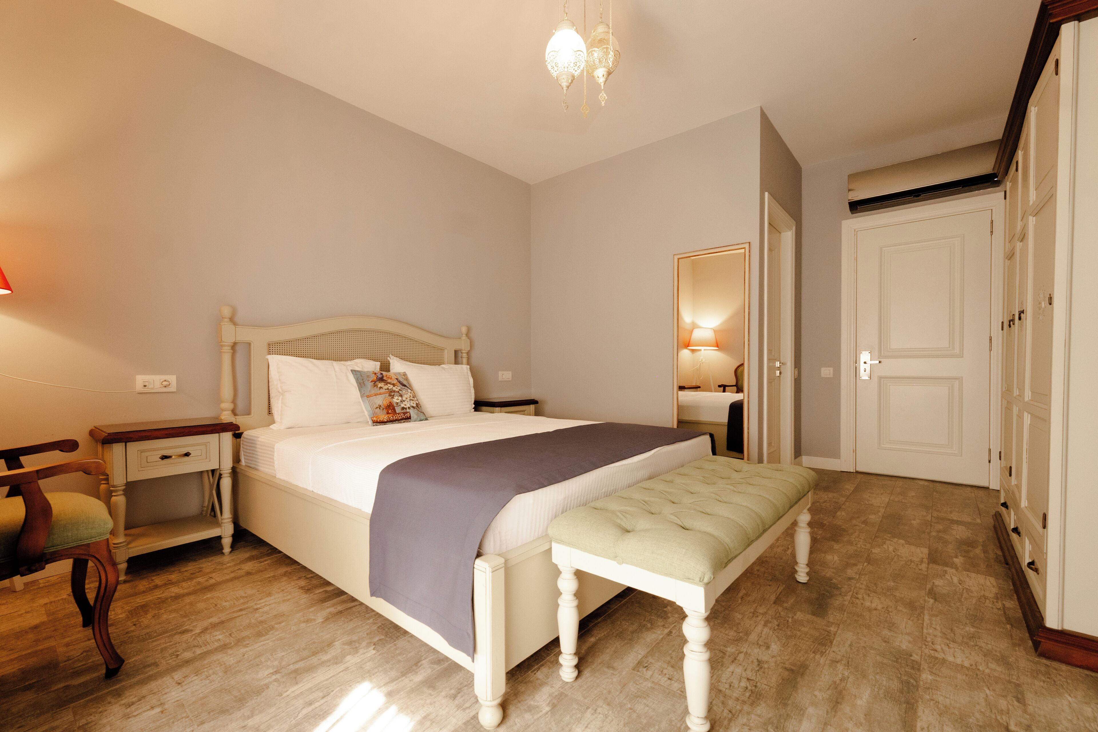Une chambre à coucher comprenant un lit, des tables de chevet, un banc, un miroir et une armoire.
