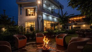 A modern building with a fire pit in the courtyard, surrounded by wicker chairs. - River View Resort (Haridwar)