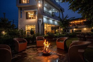A modern building with a fire pit in the courtyard, surrounded by wicker chairs. - River View Resort (Haridwar)