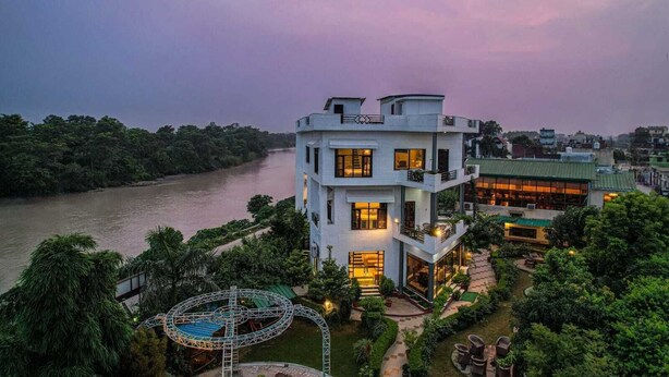 A multi-story hotel with a river view, a pool, and a well-maintained garden. - River View Resort (Haridwar)