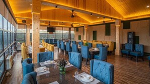 A restaurant with wooden ceilings, blue upholstered chairs, and a long dining table. - River View Resort (Haridwar)