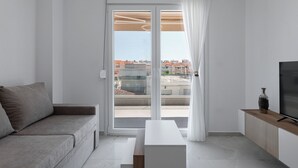 Una sala moderna con un sofá, una mesa de centro, un televisor y un ventanal corredero que da a un balcón exterior.