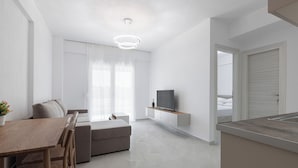 Una sala de estar moderna con un sofá, una mesa de comedor, un televisor y una zona de cocina.