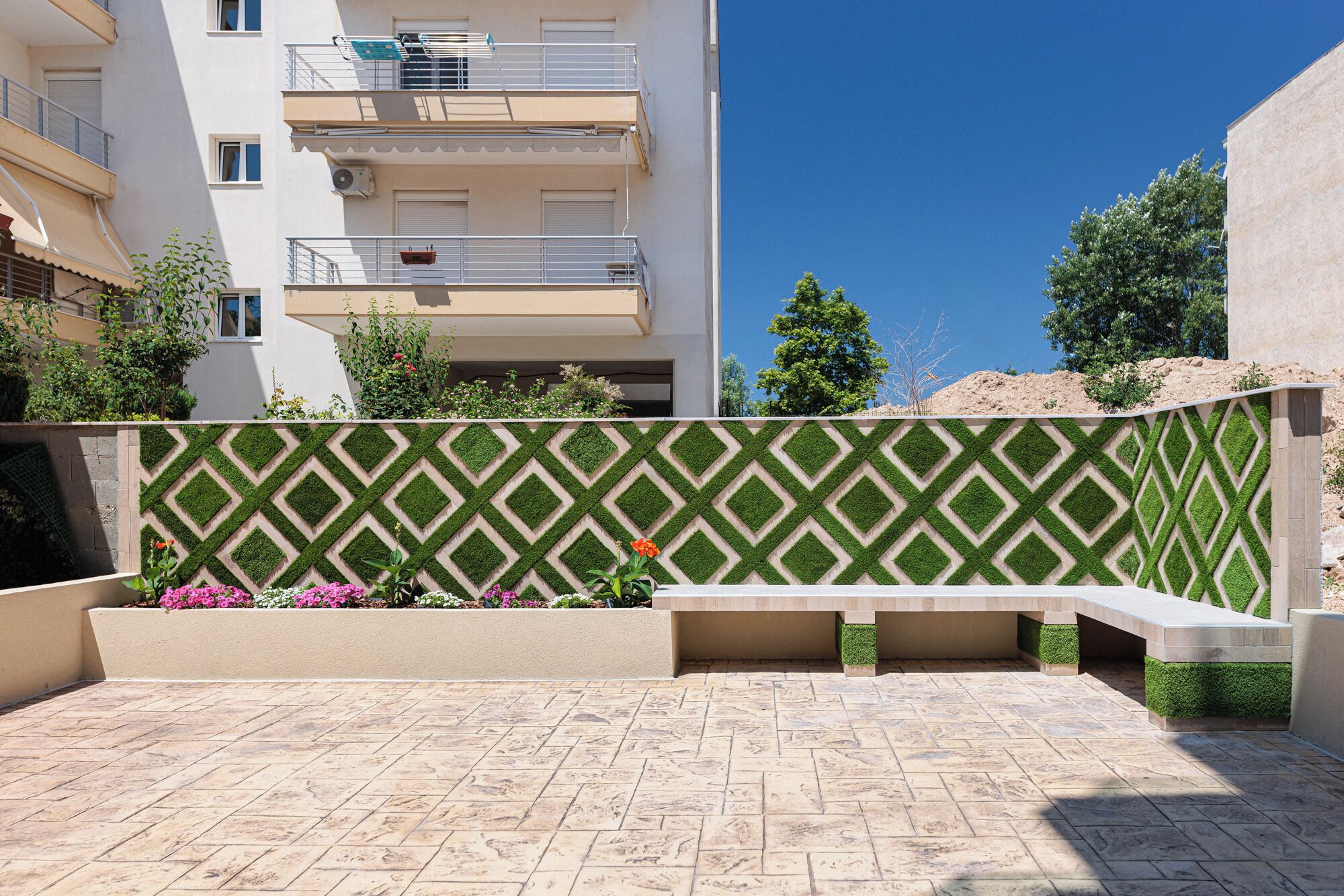 A courtyard with a patterned wall, a bench, and a building in the background.