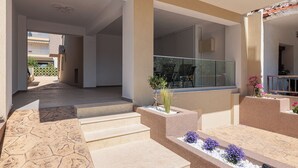 Un espacio moderno al aire libre con escalones que conducen a un área de estar cubierta, un pequeño jardín y vistas a un edificio con puertas de cristal.