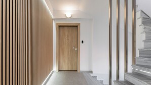 Un pasillo con una puerta de madera, un aplique encima y una escalera de mármol a la derecha.