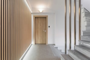A hallway with a wooden door, a light fixture above it, and a marble staircase to the right. - Adriana Suites Nea Kallikratia (Kallikrateia)