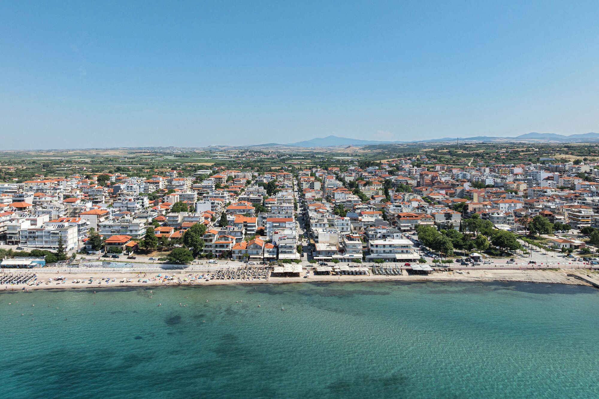 Vista aérea de una ciudad costera con edificios residenciales densos, una playa y aguas azules y cristalinas.