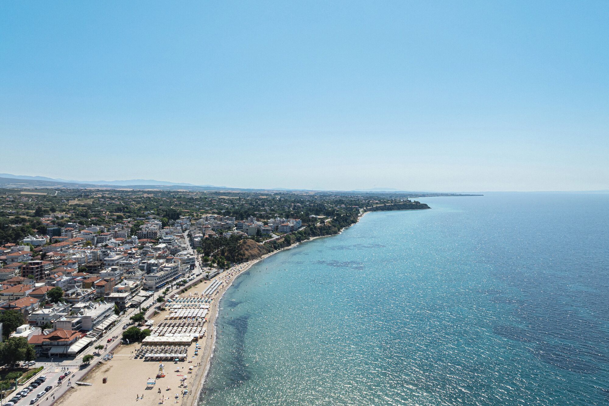 Une vue aérienne d’une ville côtière, avec une plage, des bâtiments et un ciel dégagé.