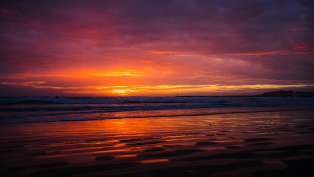 Ein Strand bei Sonnenuntergang mit Wellen und bewölktem Himmel.