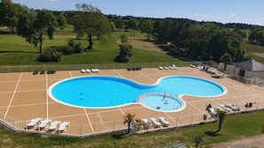 Ein Schwimmbecken mit wellenförmigem Design, umgeben von Liegestühlen und einem eingezäunten Bereich.