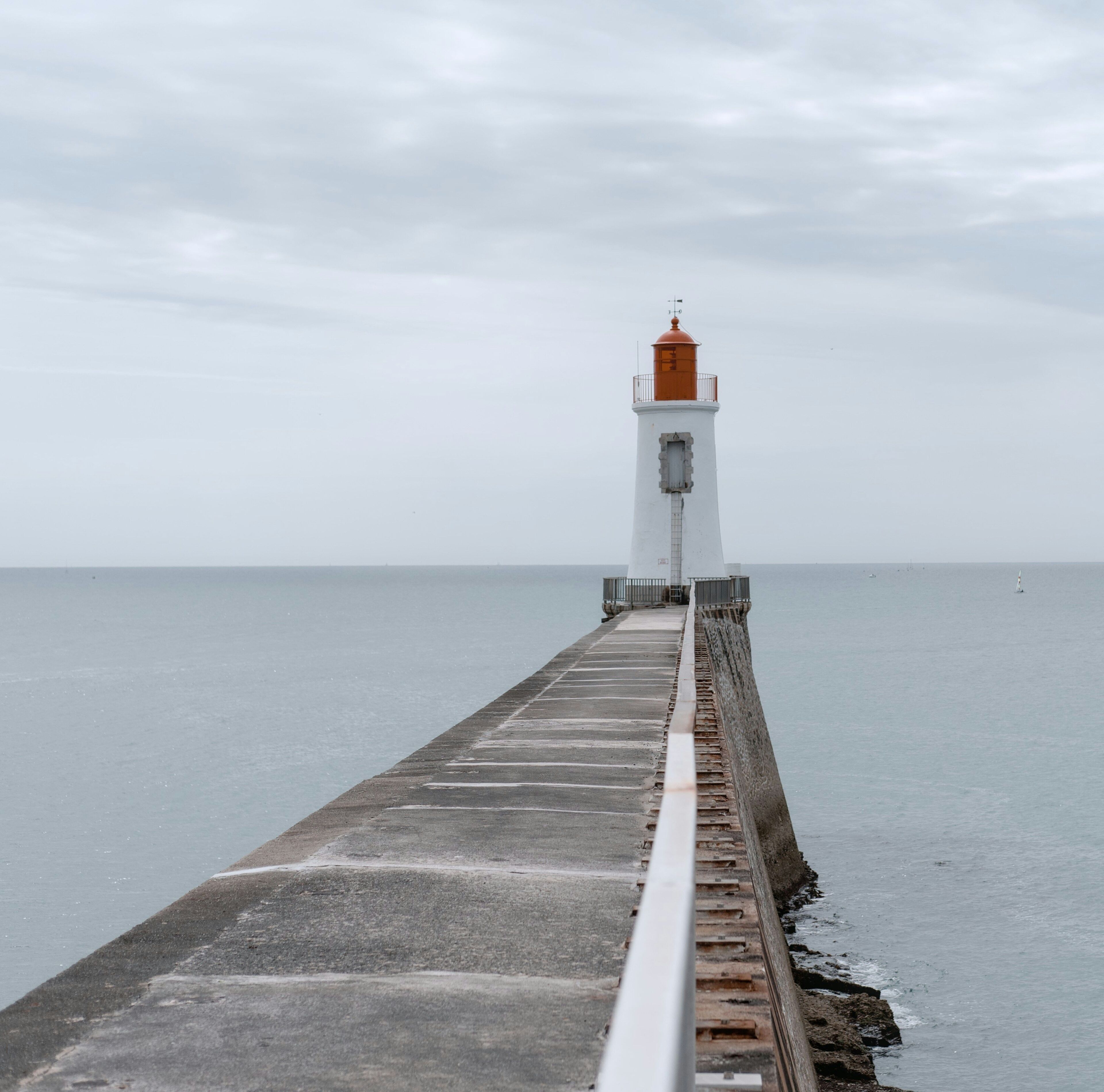 Ein Leuchtturm, der sich ins Meer erstreckt, mit einem Betonweg, der zu ihm führt.