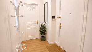 Un couloir avec un porte-manteau, une plante en pot, une porte avec une serrure et un tableau encadré accroché au mur.