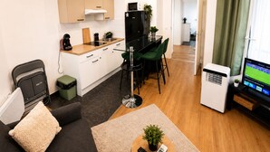 Un espace de vie compact comprenant un coin cuisine, un coin repas, un espace détente avec un canapé et des fauteuils, et un téléviseur.