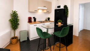 Une cuisine compacte équipée d’un four à micro-ondes, d’un réfrigérateur et d’un petit coin repas avec deux chaises vertes.