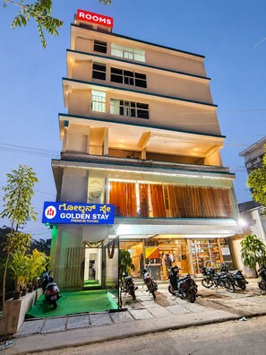 Un hotel de varios pisos con un letrero que indica 'GOLDEN STAY PREMIUM ROOMS' y un cartel que dice 'HABITACIONES' encima.