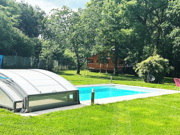 A swimming pool with a glass enclosure, surrounded by green grass and trees.