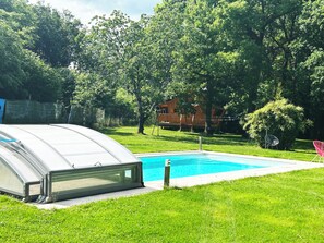 Piscina com cobertura de vidro, rodeada por grama verde e árvores.