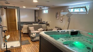 Een ruimtelijk ogende spa met een bubbelbad, rieten meubels, een glazen douchecabine en een plafondprojector.