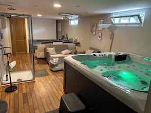 A spa-like room with a hot tub, wicker furniture, a glass shower enclosure, and a ceiling projector.