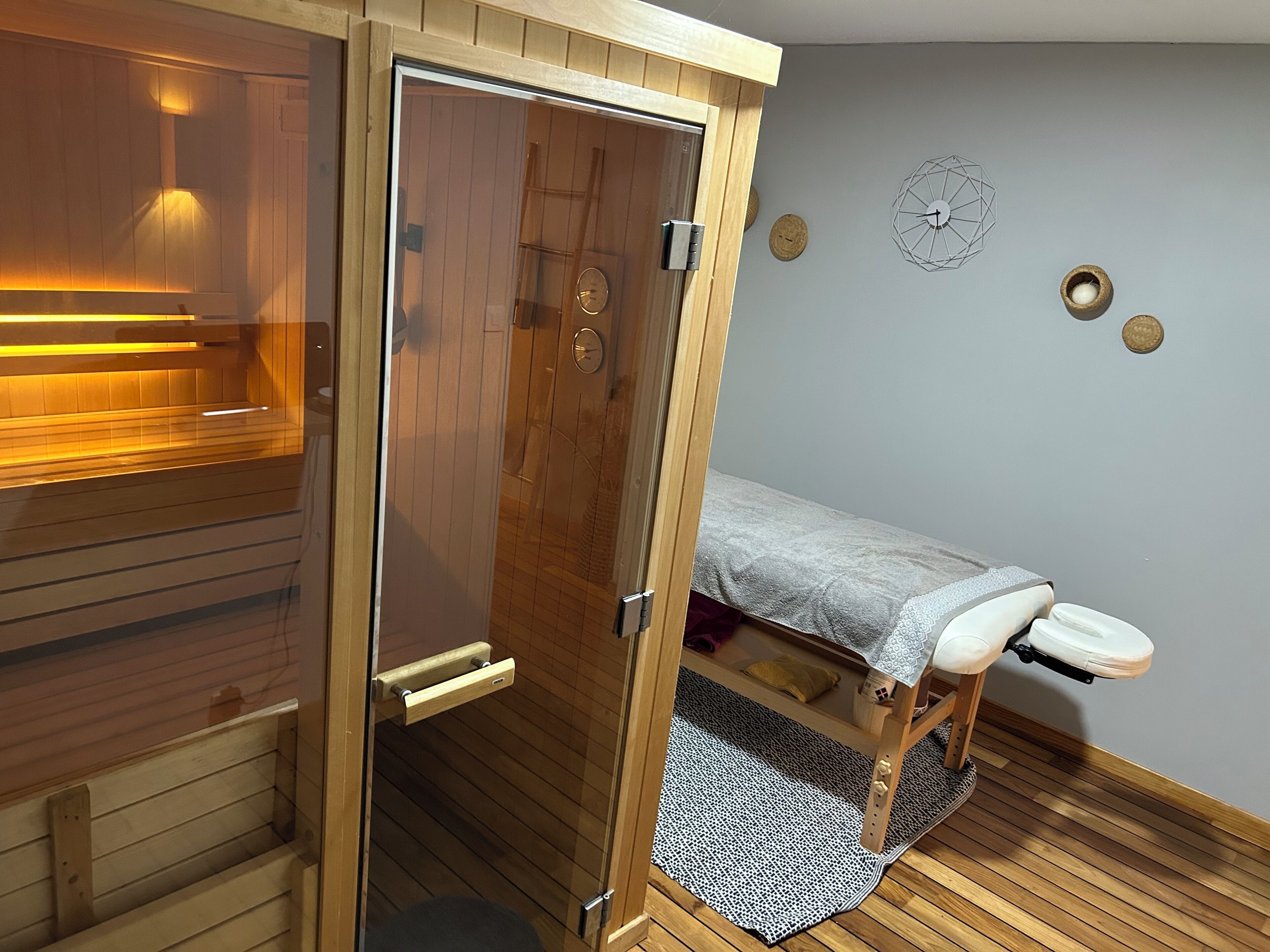 Ein Zimmer mit Holzboden, einer Sauna, einem Bett mit weißer Bettdecke, einer Wanduhr und einem kleinen Teppich.