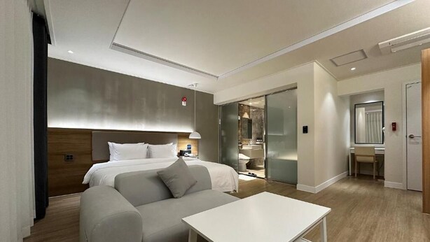 Una habitación de hotel moderna con una cama, un sofá, una mesa y un baño visible a través de una puerta de cristal.