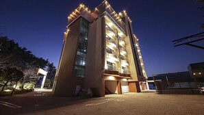 Un edificio de varios pisos con balcones, zona de estacionamiento y entrada protegida por un portón.