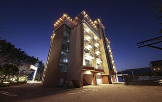 A multi-story building with balconies, a parking area, and a gated entrance.