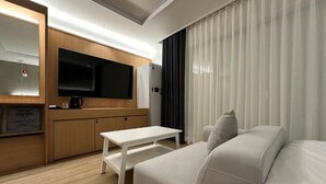 Una habitación de hotel moderna con sofá, televisor de pantalla plana, cafetera y mueble de madera.