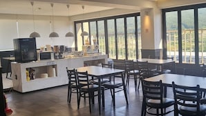 Un restaurante con mesas y sillas, una barra con electrodomésticos y amplios ventanales con vistas.