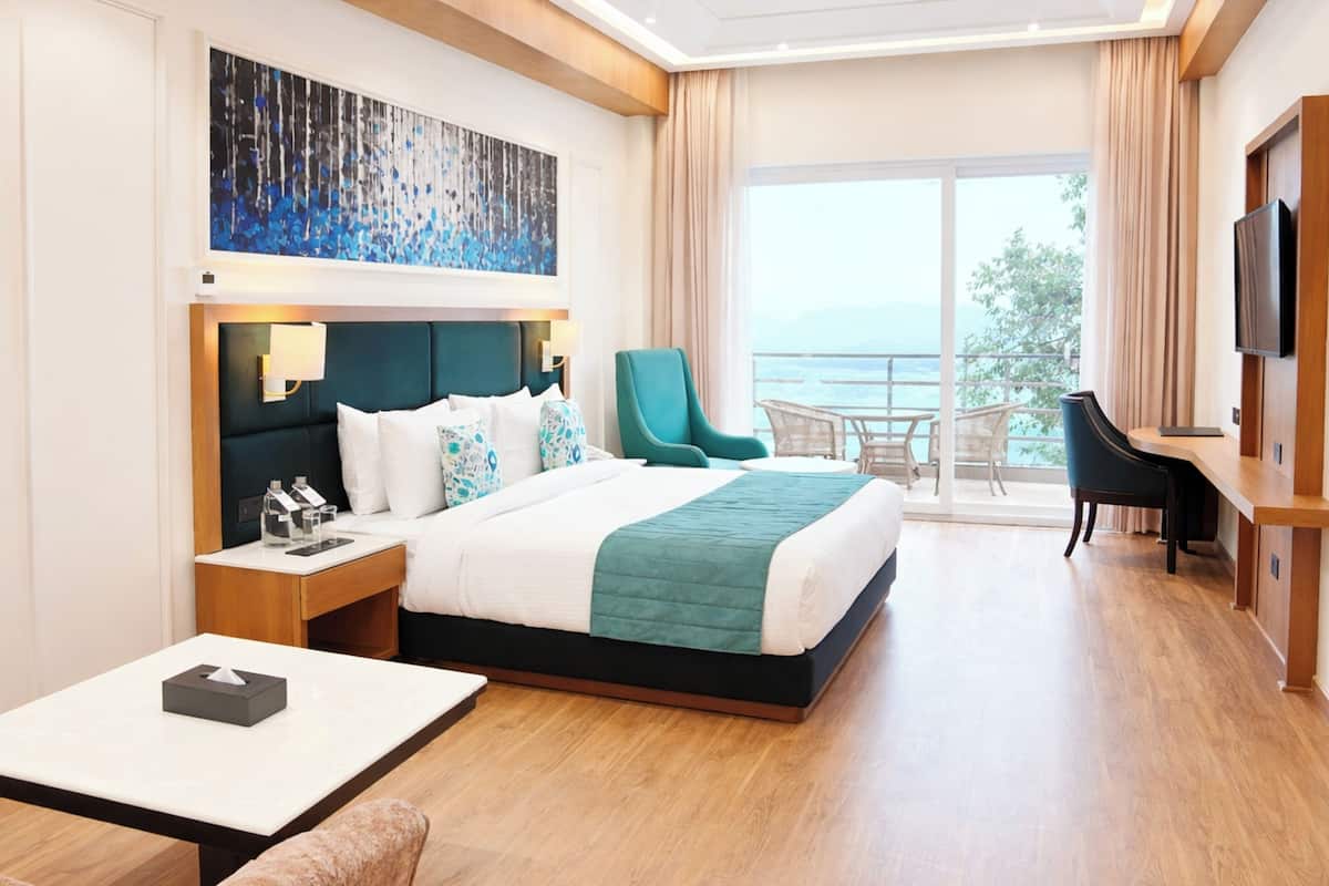 A hotel room with a bed, a chair, a TV, a table, and a balcony with a view.