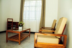 A room with a glass-top table, two wooden chairs with cushioned seats, a wooden chair, and a vase with flowers.
